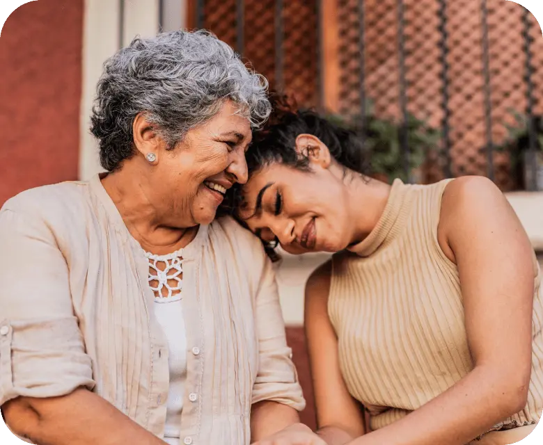 An older woman and younger woman smiling and leaning their heads together.
