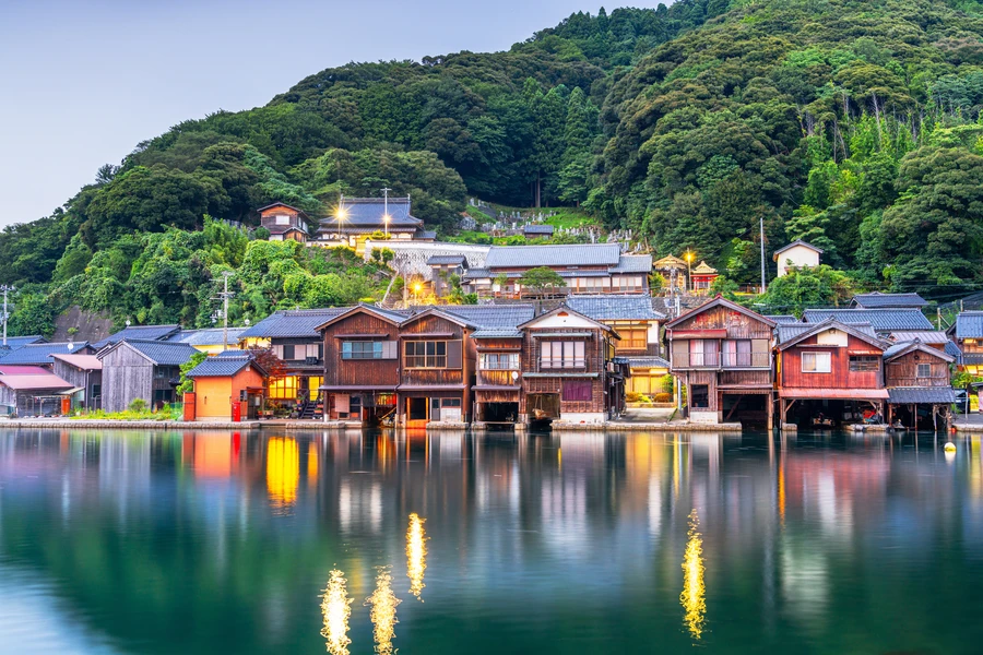 Historic funaya boathouses at Ine Bay, Kyoto, reflected in calm water at dusk.