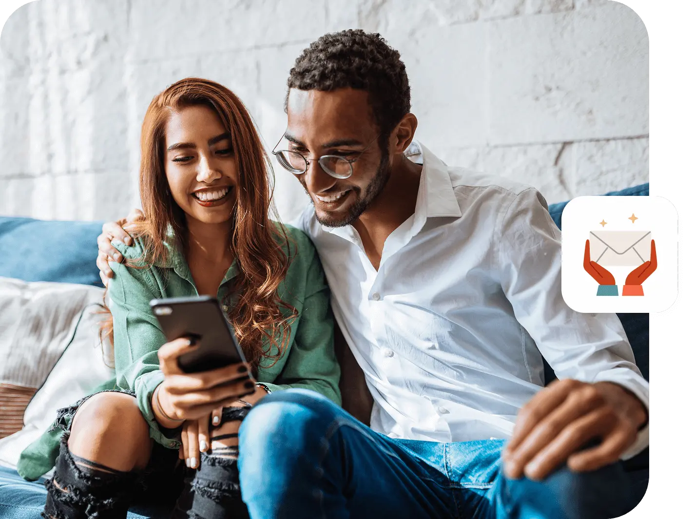 A smiling couple sits on a couch looking at a phone together.