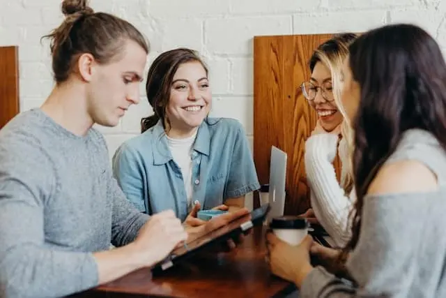 Four friends smile and talk around a café table with coffee.
