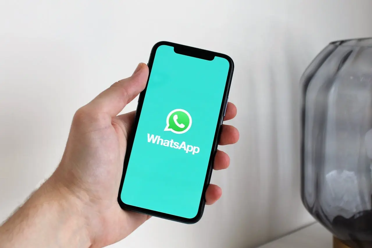 Persona que sostiene un celular en el que se ve el logotipo de WhatsApp.