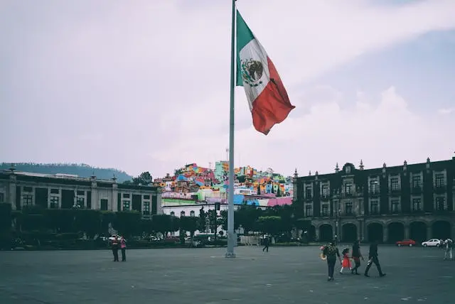 People in a large plaza with a tall Mexican flag.