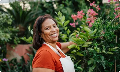 Mujer sonriendo mientras está de pie en un jardín, al aire libre.