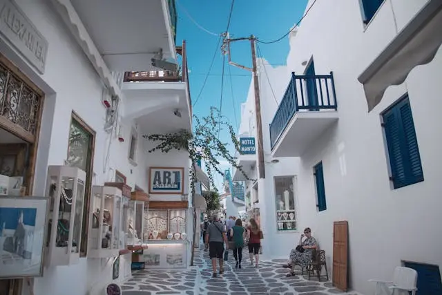 People walking along a bright market street lined with white buildings.