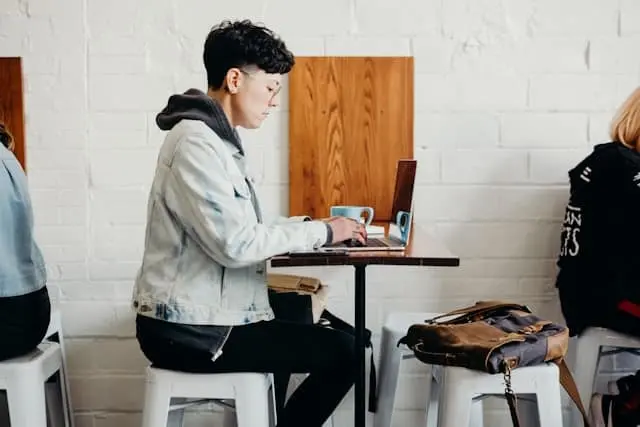 A person in a denim jacket works on a laptop at a small café table.