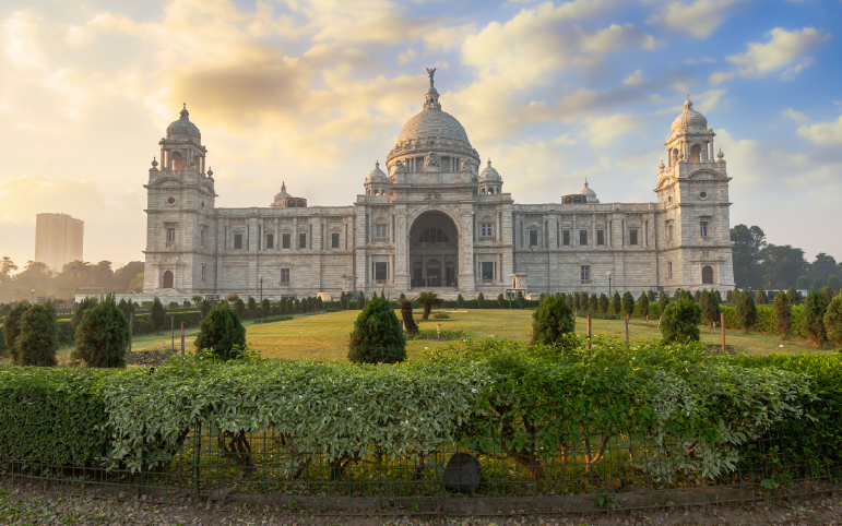 Victoria Memorial in Kolkata, India, with its white marble architecture surrounded by gardens under a partly cloudy sky at sunset.