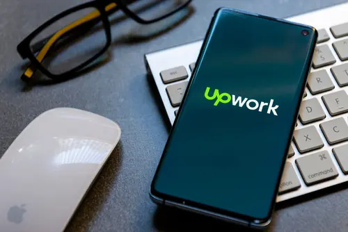 A smartphone displays the Upwork app beside a keyboard and glasses.