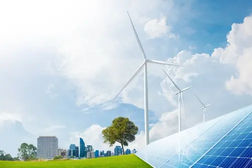 Wind turbines and solar panels stand in a green field with a city skyline in the background.
