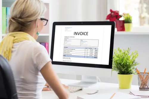 A woman views an invoice displayed on a desktop computer screen.